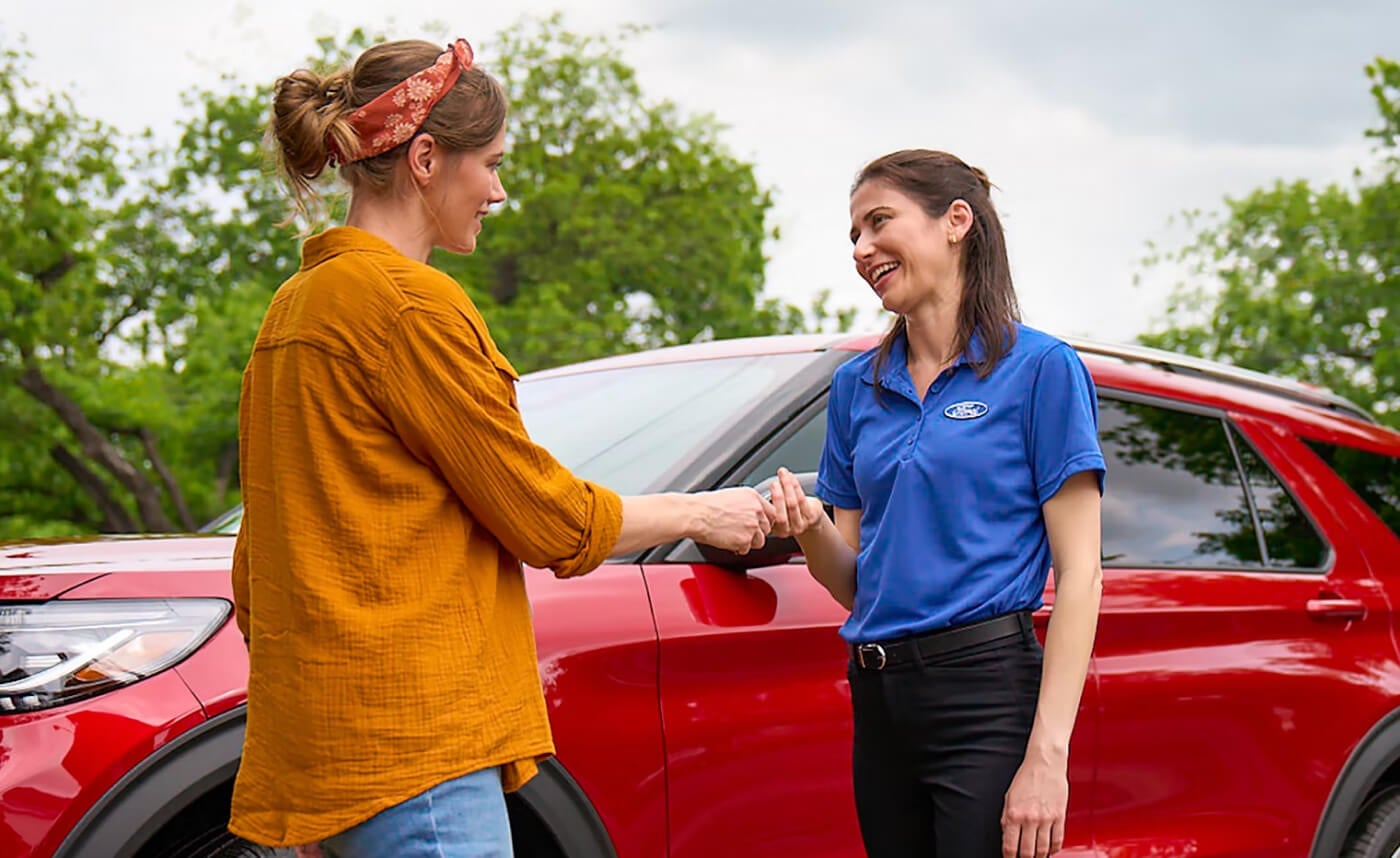A Ford employee hands a woman keys to a red Ford Explorer, seen parked behind them.