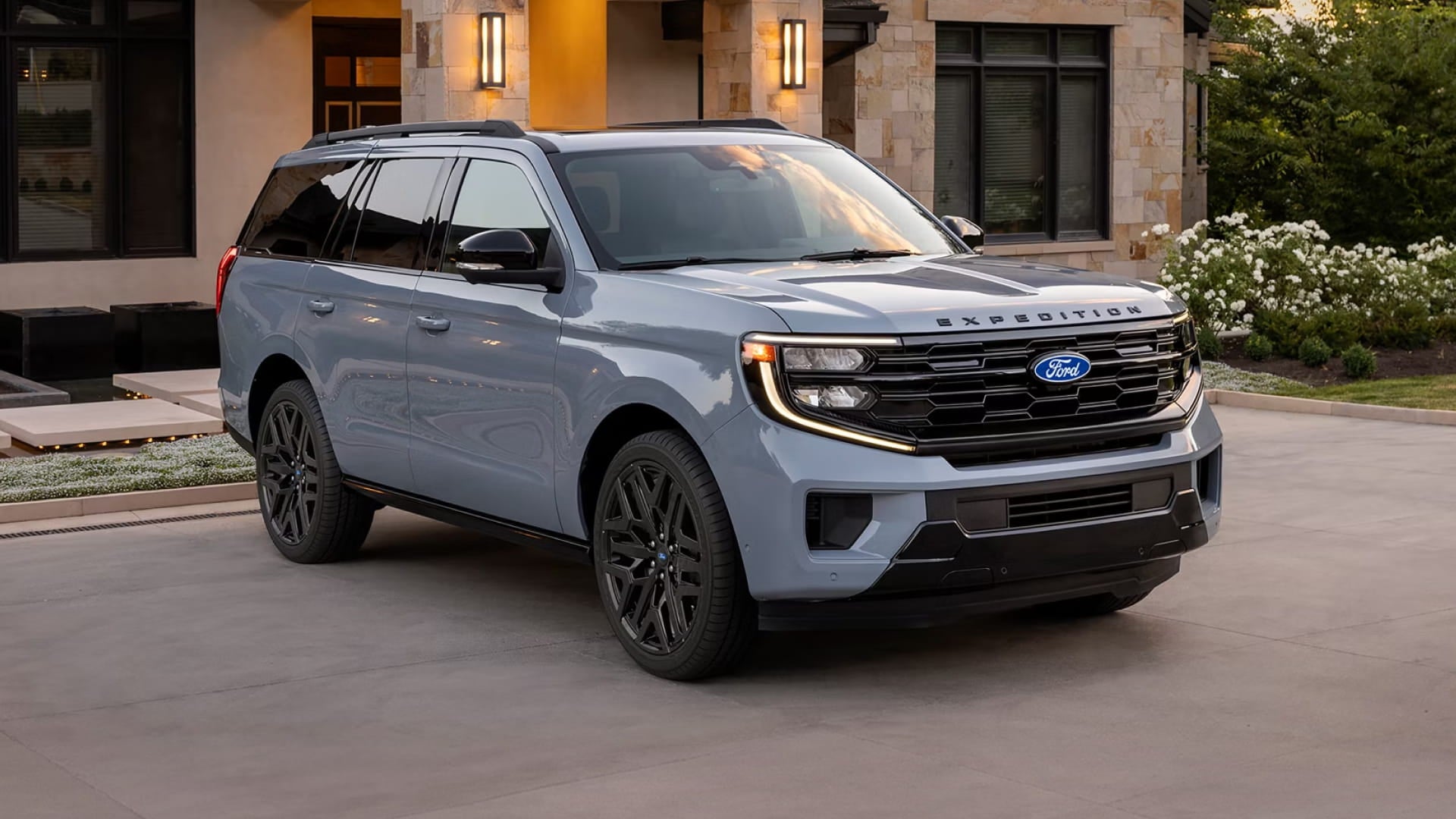 Front three-quarter view of a light blue Ford Expedition parked in the driveway of a modern home.